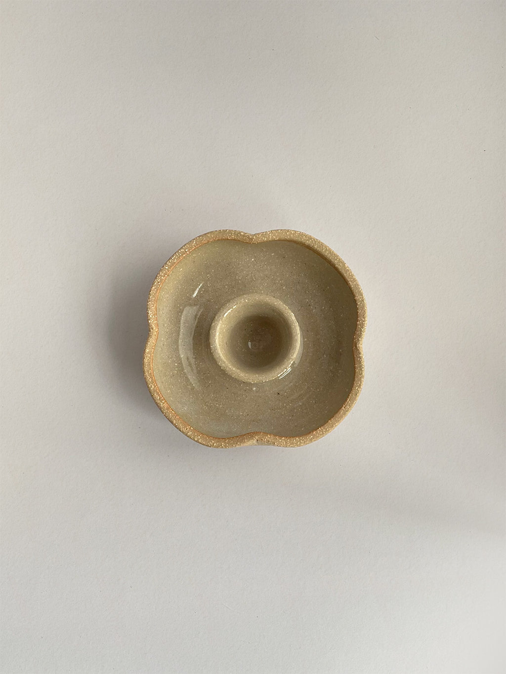 A hand-thrown ceramic candle holder in a rustic natural glaze on a neutral background - top view.