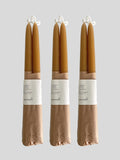 Three pairs of beeswax hand-dipped taper candles in a natural honey colour, wrapped in brown kraft paper with a white paper label, against a solid light neutral background.