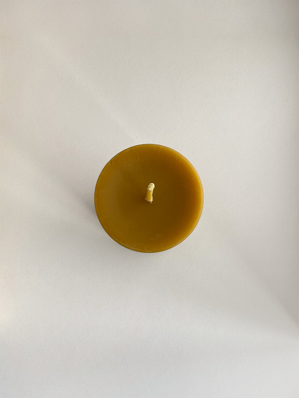 Organic beeswax pillar candle on a neutral background - top view.