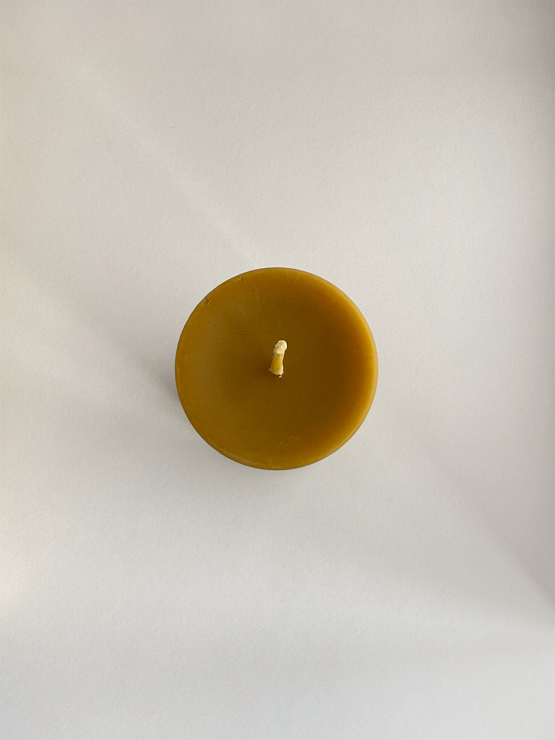 Organic beeswax pillar candle on a neutral background - top view.