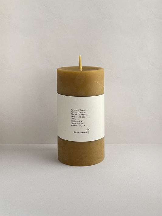 Organic beeswax pillar candle with label on a neutral background - front view.