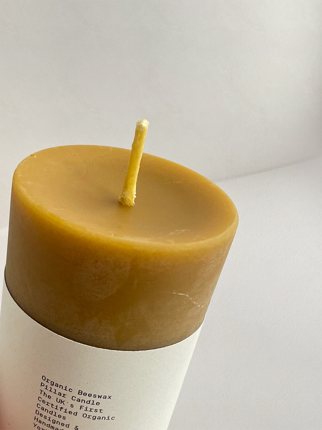 Close-up detail of organic beeswax pillar candle with label on a neutral background.