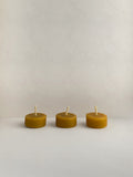 Three organic beeswax tealight candles on a light surface.