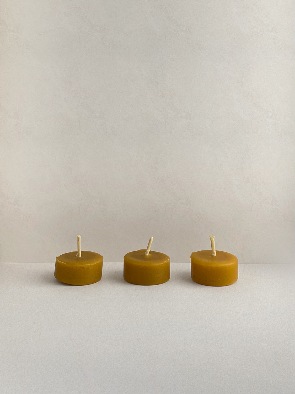 Three organic beeswax tealight candles on a light surface.