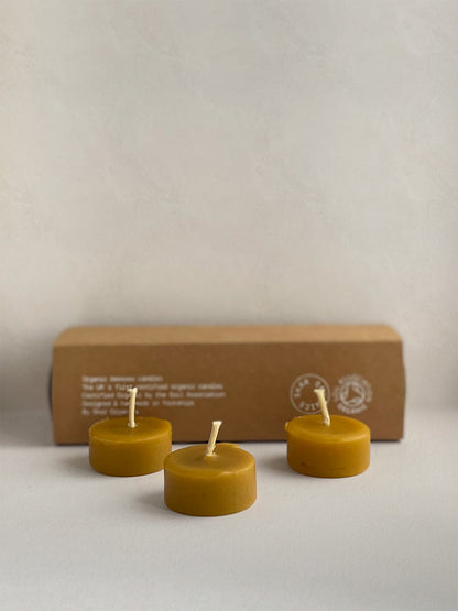Three organic beeswax tealight candles in front of box on a light surface.