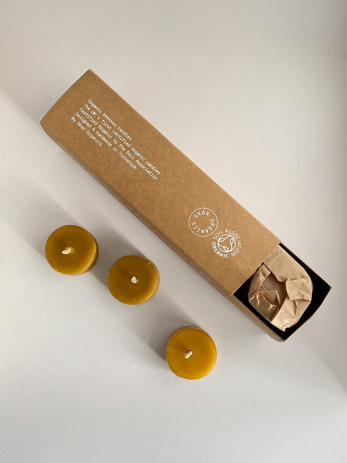 Three organic beeswax tealight candles next to box on a light surface - top view.