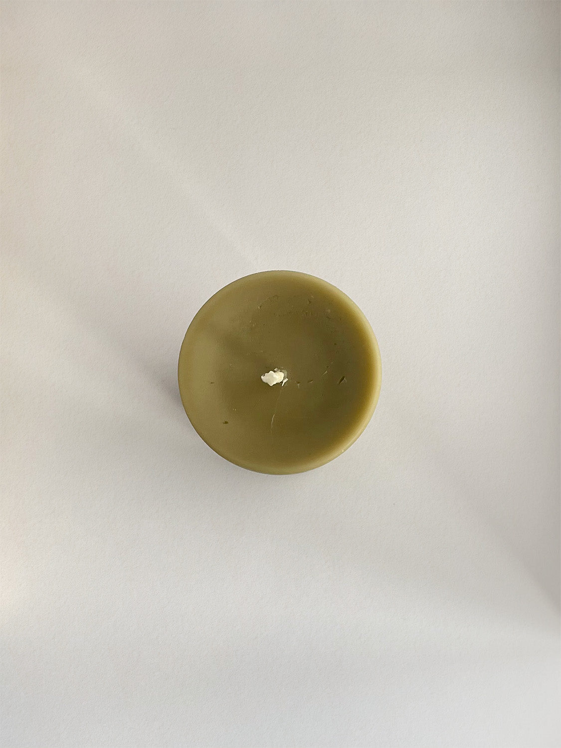 Organic beeswax & green tea pillar candle on a neutral background - top view.