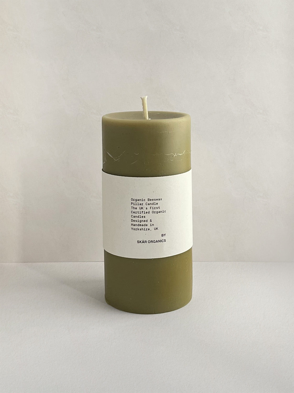 Organic beeswax & green tea pillar candle with label on a neutral background - front view.