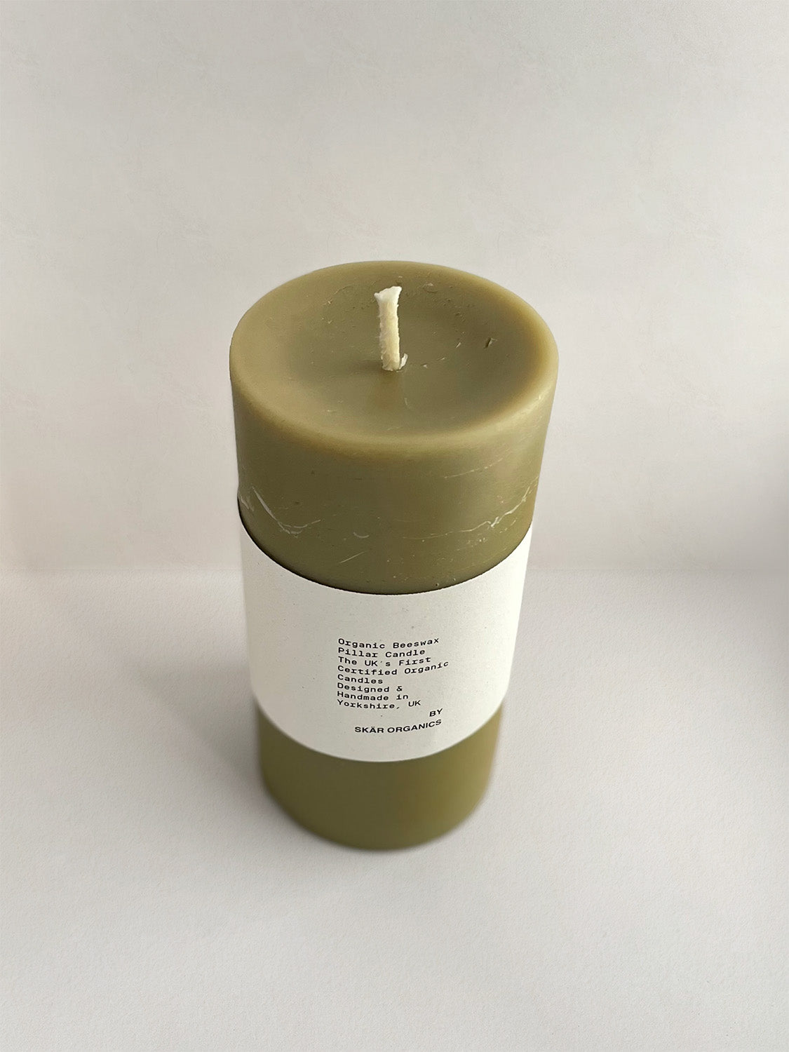 Organic beeswax & green tea pillar candle with label on a neutral background - front view 2.