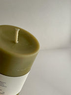 Close-up detail of organic beeswax & green tea pillar candle with label on a neutral background.