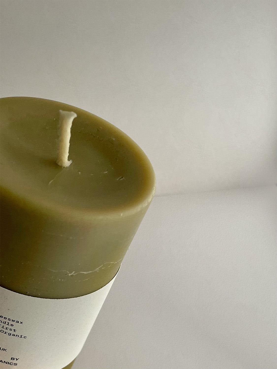 Close-up detail of organic beeswax & green tea pillar candle with label on a neutral background.