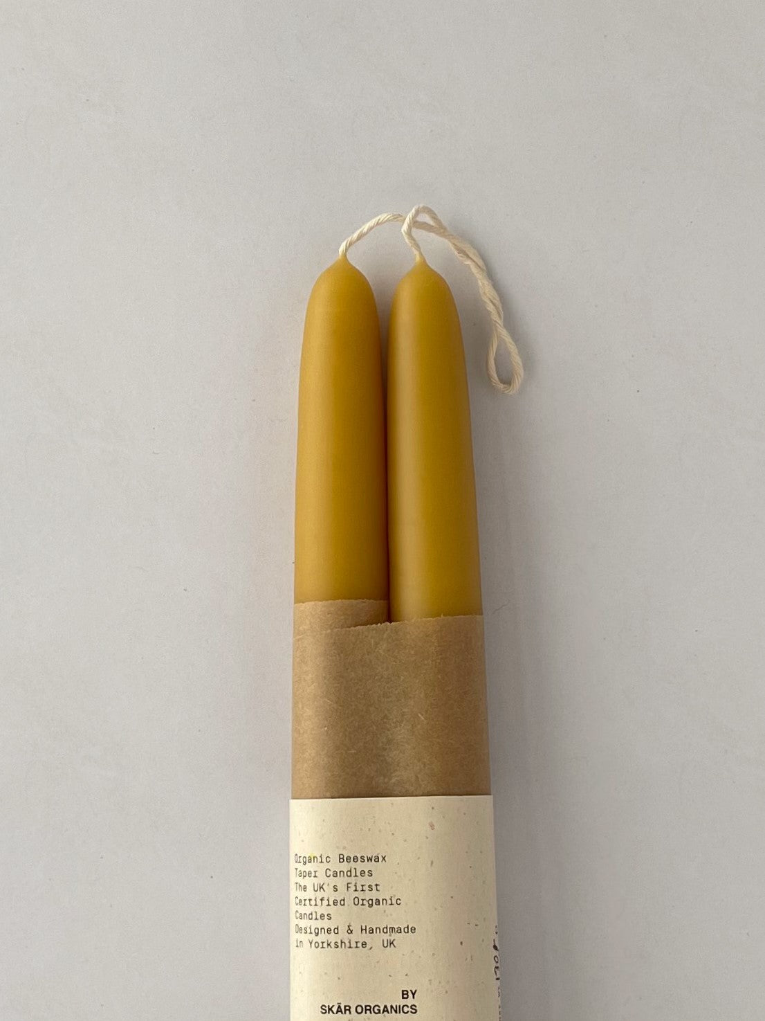 Pair of organic beeswax hand-dipped taper candles on a light background - detail.