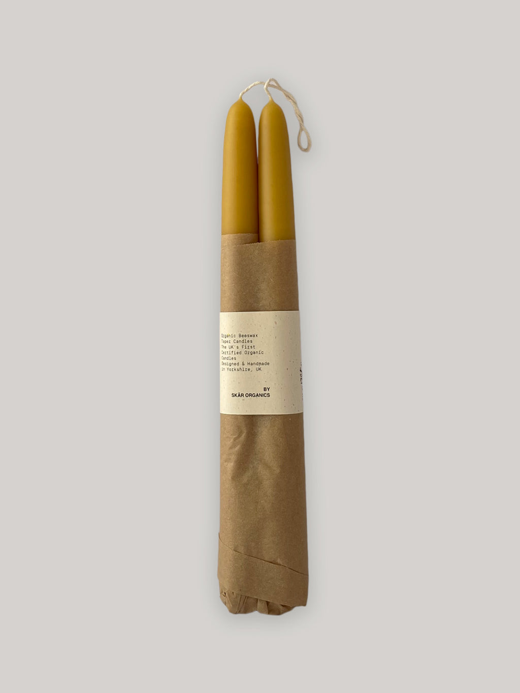 Pair of organic beeswax hand-dipped taper candles on a neutral background - front view.