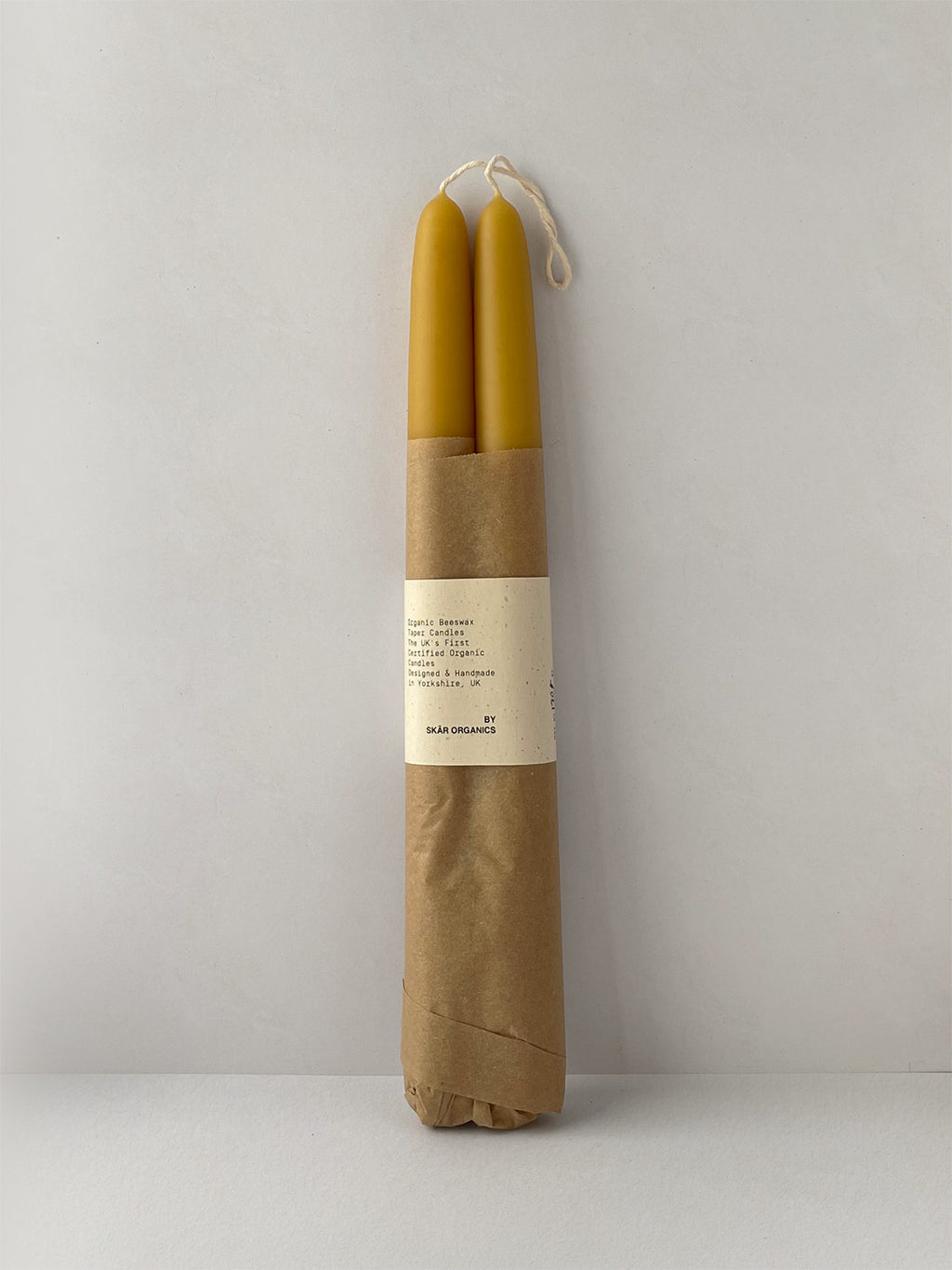 Pair of organic beeswax hand-dipped taper candles on a light surface - front view.