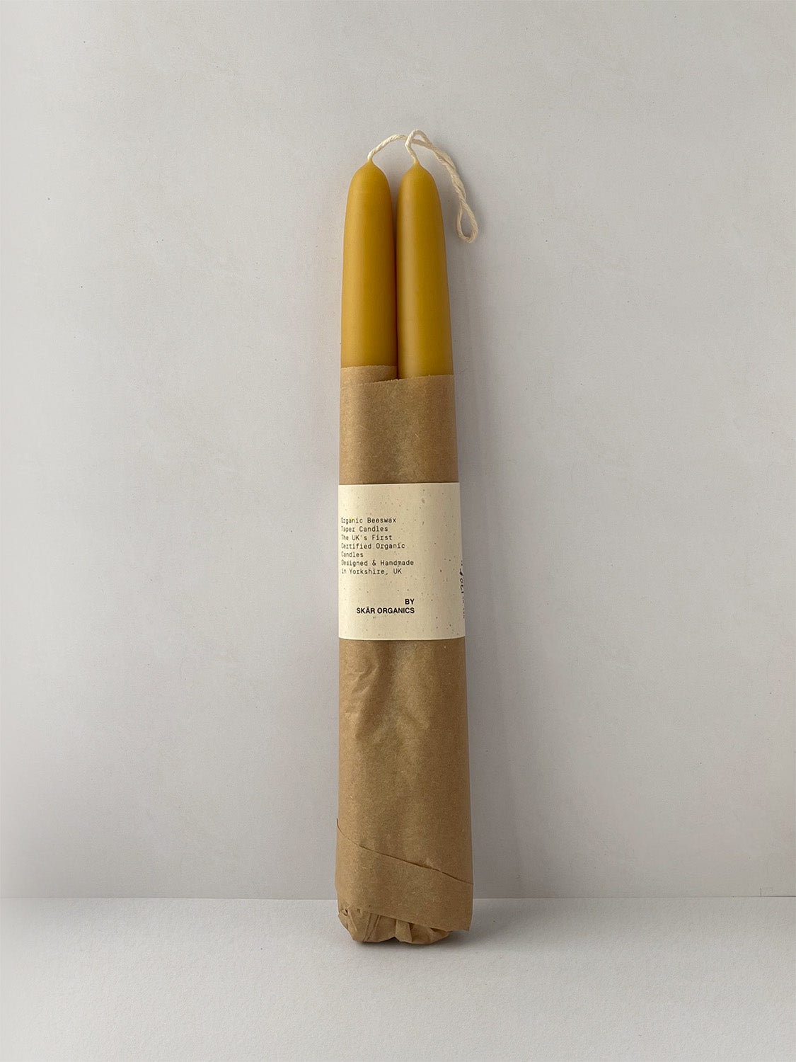 Pair of organic beeswax hand-dipped taper candles on a light surface - front view.