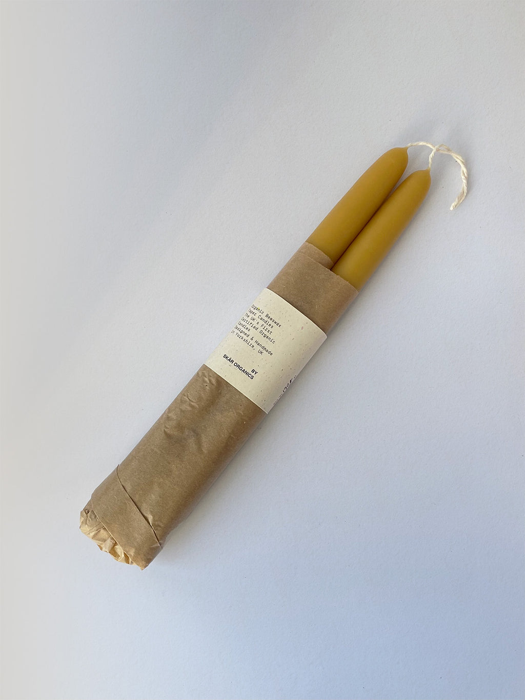 Pair of organic beeswax hand-dipped taper candles on a light surface - top view.