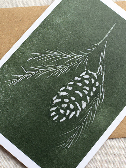 Close-up of botanical Christmas card with pine cone and branch design on a green background.