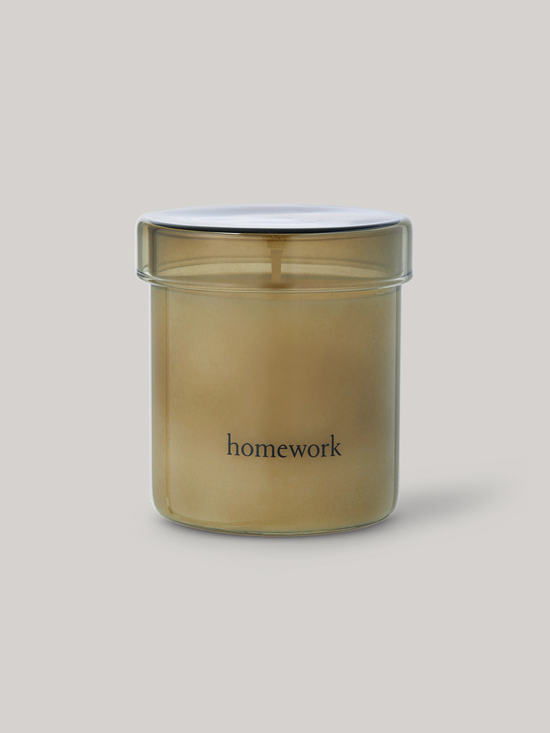Candle in smoked glass jar labelled 'homework' on a neutral background.