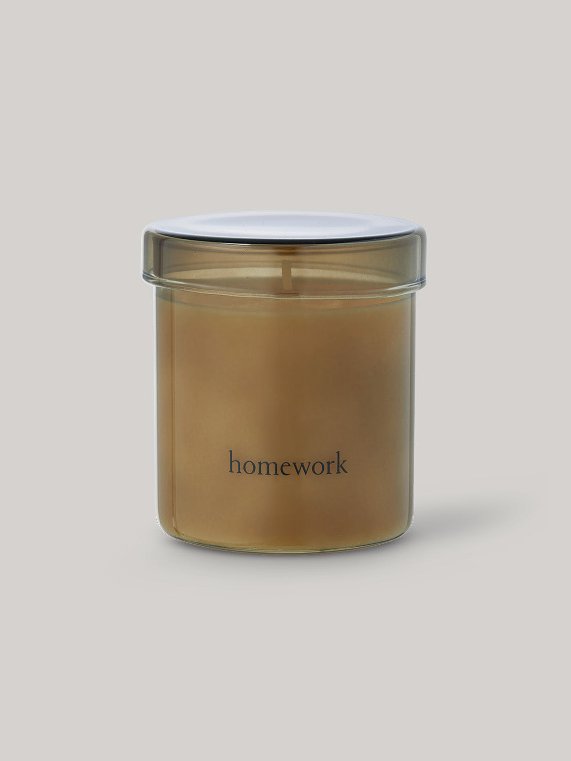 Candle in smoked glass jar labelled 'homework' on a neutral background.