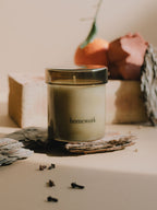 Candle in smoked glass jar labelled 'homework' on a surface with decorative elements.