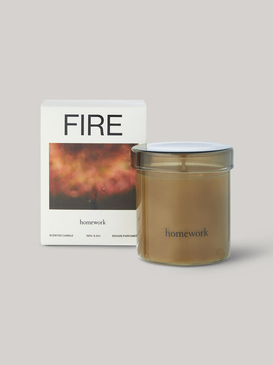 Candle in smoked glass jar labelled 'homework' with packaging titled 'FIRE' on a neutral background.