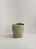 A handmade ceramic coffee cup with a rustic glaze finish, showing speckling and unique finger marks from the making process - back view.