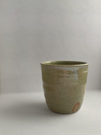 A handmade ceramic coffee cup with a rustic glaze finish, showing speckling and unique finger marks from the making process - detail.