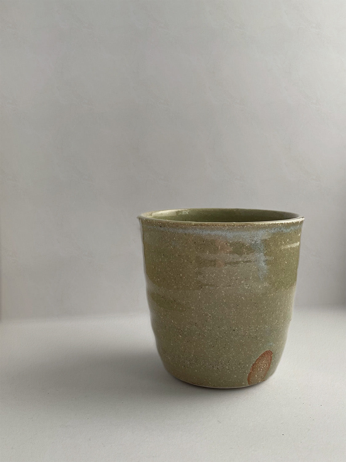 A handmade ceramic coffee cup with a rustic glaze finish, showing speckling and unique finger marks from the making process - detail.