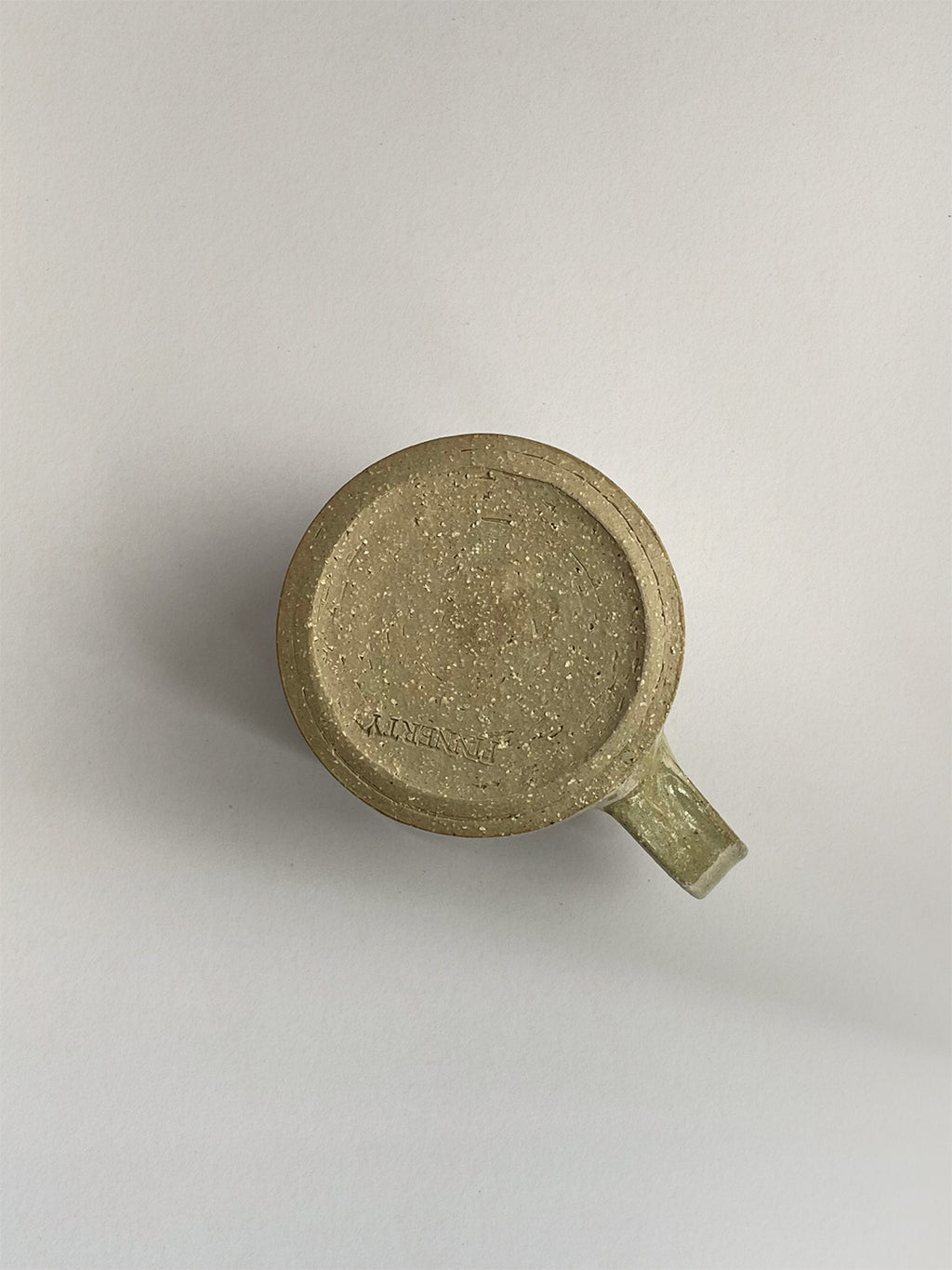 A rustic light green handmade ceramic espresso mug with a handle, on a neutral background - base view.