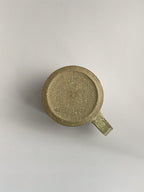 A rustic light green handmade ceramic espresso mug with a handle, on a neutral background - base view.