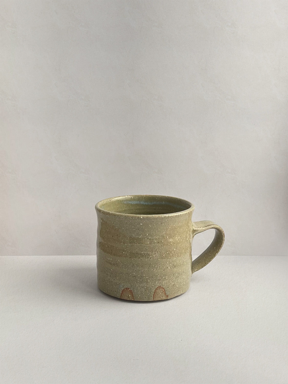 A rustic light green handmade ceramic espresso mug with a handle, on a neutral background - left side view.