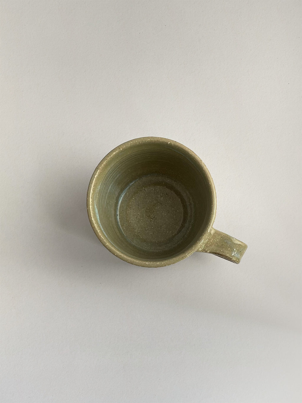 A rustic light green handmade ceramic espresso mug with a handle, on a neutral background - top view.