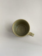 A rustic light green handmade ceramic espresso mug with a handle, on a neutral background - top view.