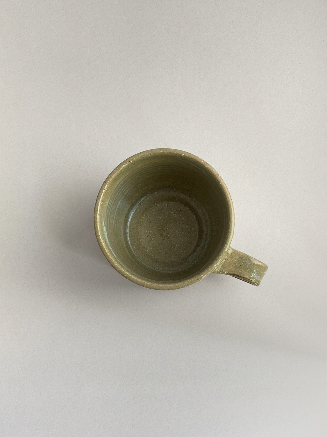 A rustic light green handmade ceramic espresso mug with a handle, on a neutral background - top view.