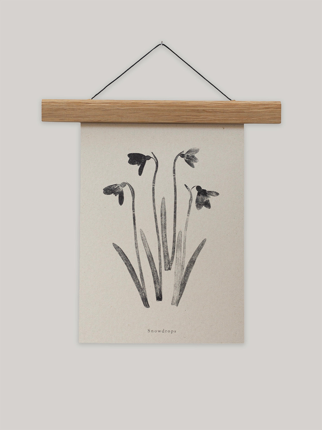 Botanical art print of snowdrops on a beige background with a wooden hanger.