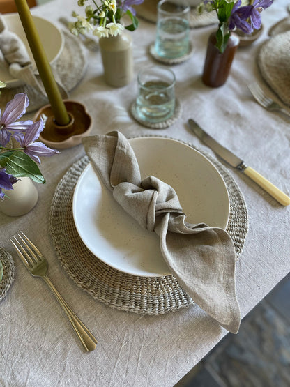 Elegant table setting with a white bowl, linen napkin, and decorative elements on a light-coloured tablecloth.
