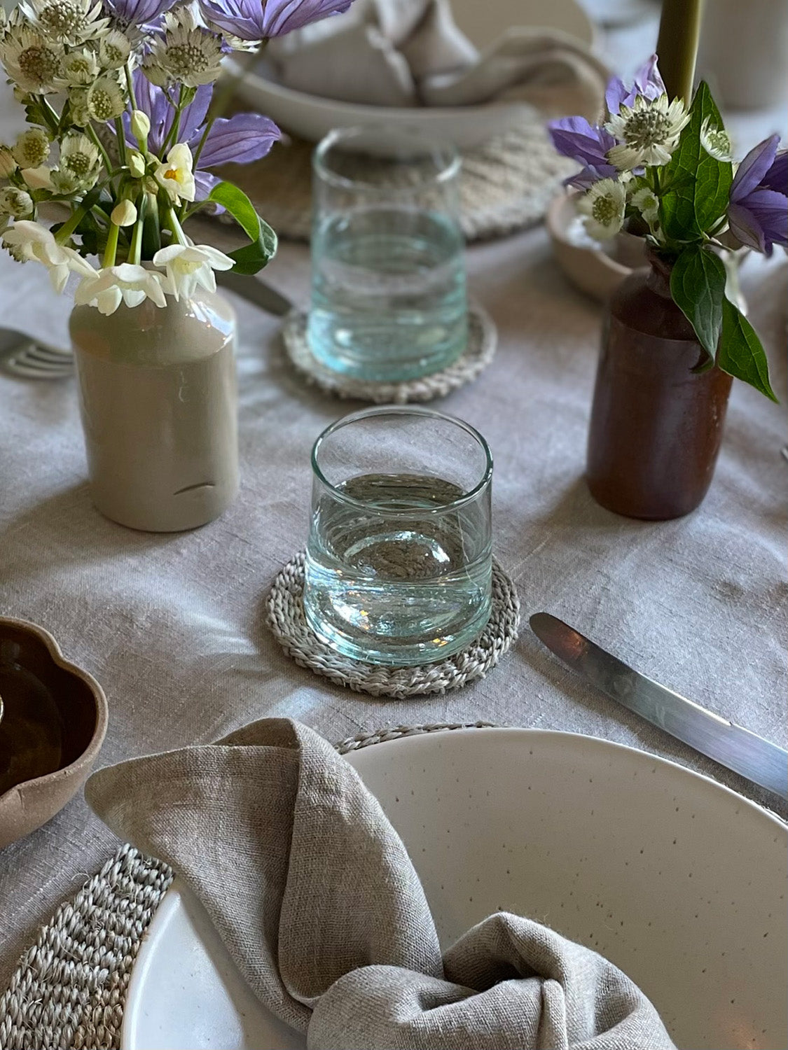 Table setting with glasses, flowers, and linen napkins on a light-coloured tablecloth.