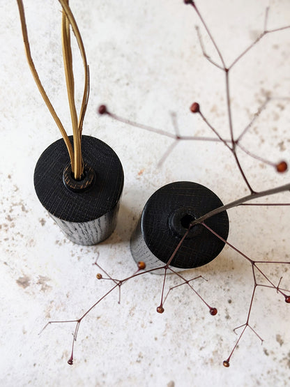 Pair of straight bud vases in ebonised Oak with dried stems, on a mottled off-white surface - top view.