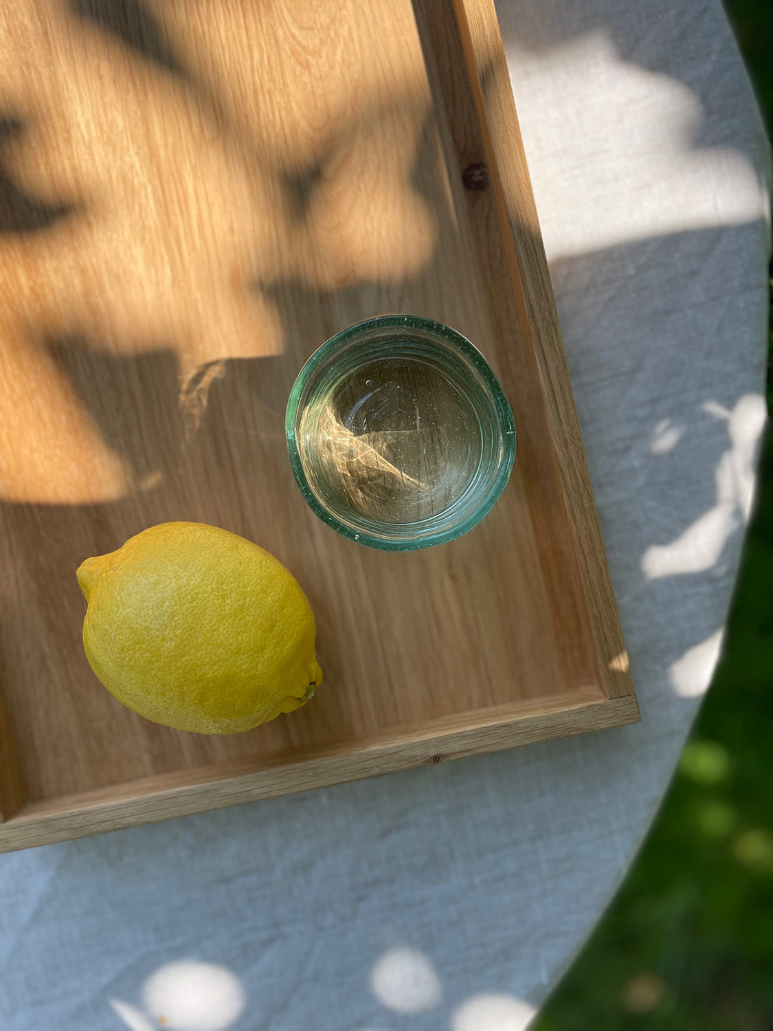A handmade recycled glass tumbler and lemon and on a wooden tray outdoors.