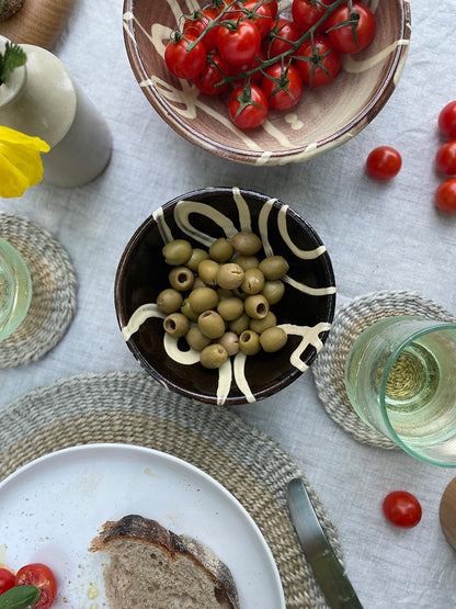 Table setting with a bowl of olives, bread, and tomatoes on a linen tablecloth.