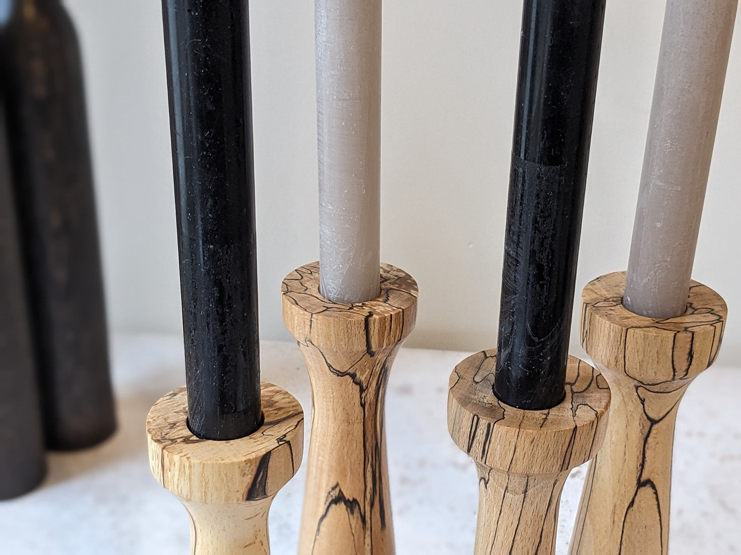 Two pairs of tall, tapered wooden candle holders in Spalted Beech with candles - detail.