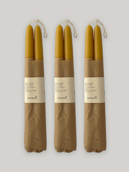 Three pairs of beeswax taper candles wrapped in brown paper with labels on a neutral background.
