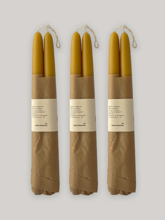 Three pairs of beeswax taper candles wrapped in brown paper with labels on a neutral background.