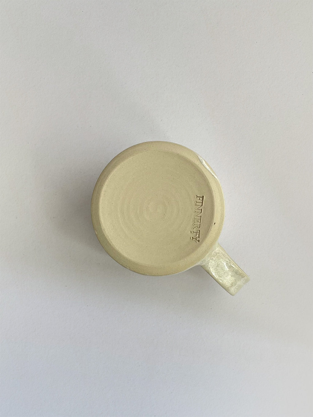 A beige handmade ceramic espresso mug with a handle, on a neutral background - base view.