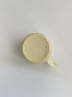 A beige handmade ceramic espresso mug with a handle, on a neutral background - base view.