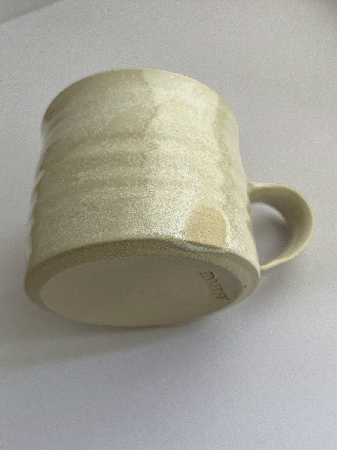 A beige handmade ceramic espresso mug with a handle, on a neutral background - detail view.