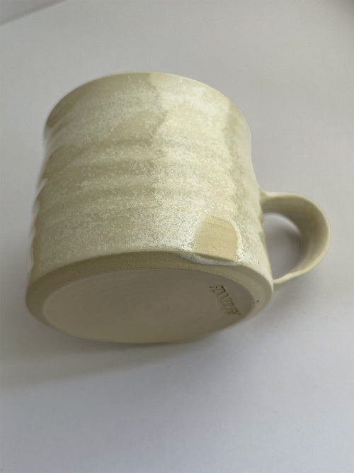 A beige handmade ceramic espresso mug with a handle, on a neutral background - detail view.