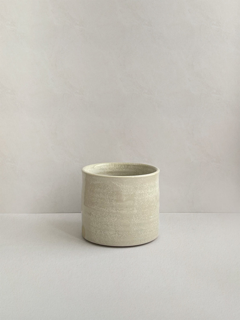 A beige handmade ceramic espresso mug on a neutral background - front view.