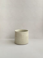 A beige handmade ceramic espresso mug on a neutral background - front view.