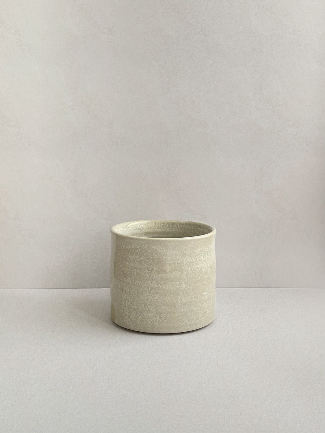 A beige handmade ceramic espresso mug on a neutral background - front view.